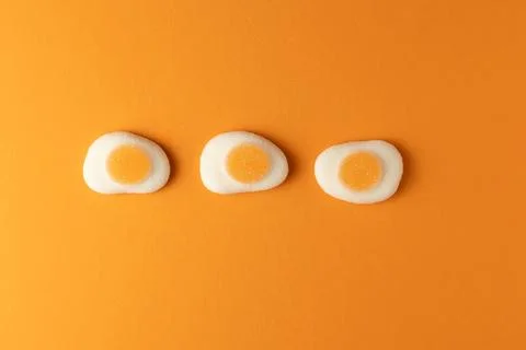 Three fried egg shaped candy on orange background representing breakfast Stock Photos