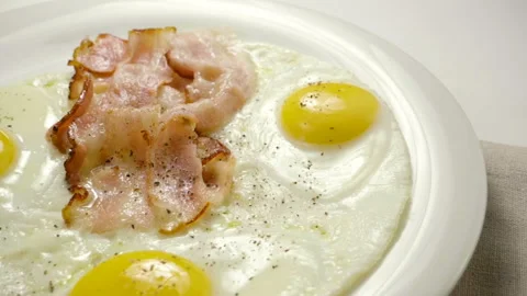 Three fried eggs and bacon serving on white plate for breakfast. Slow motion. HD Stock Footage 107435247