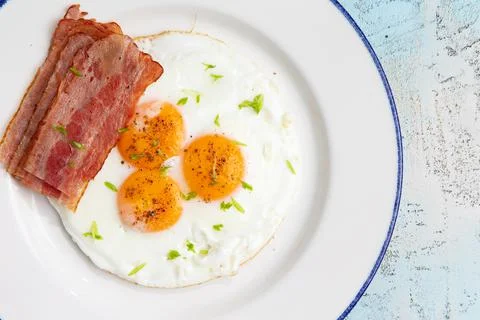 Three fried eggs with bacon in a plate Stock Photos