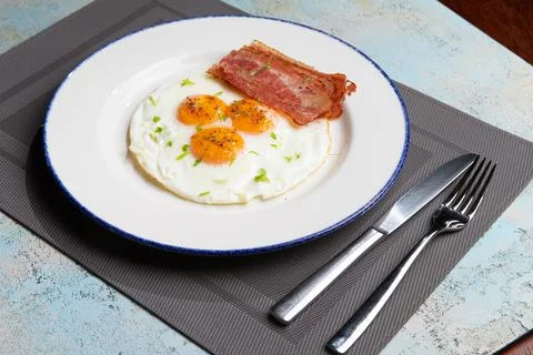 Three fried eggs with bacon in a plate Stock Photos