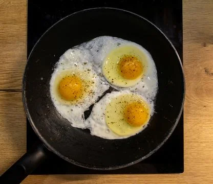 Three fried eggs cooking in pan on stove Stock Photos