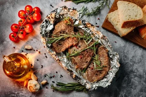 Three fried slices of beef steak in foil with rosemary, cherry tomatoes, slic Foto stock