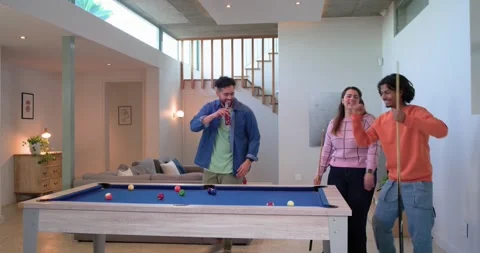 Three friends bantering and lining up shots around blue-felt pool table in Stock Footage 339272045