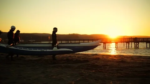 Three friends carry a kayak down the beach at sunset. Stock-Footage 88438513