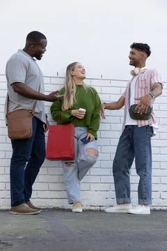 Three friends chatting while standing in front of white painted brick wall Fotos Stock