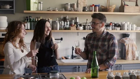 Three friends is clinking glasses and drink wine on a home kitchen party Stock Footage 73588374