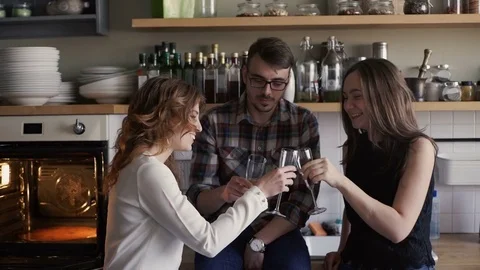 Three friends is clinking glasses and drink wine on a home kitchen party Stock Footage 73589599