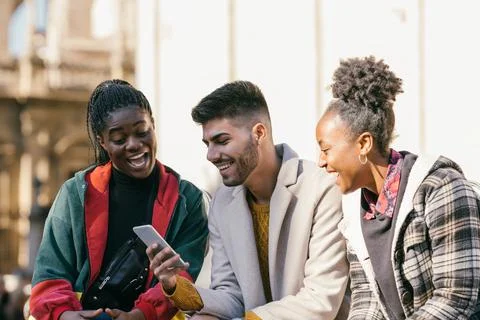 Three friends of different ethnicities looking at the mobile outdoors Stock Photos
