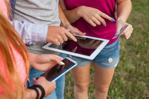 Three friends with electronic gadget in park. Close up. Stock Photos
