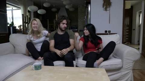 Three friends fight over the remote control at home in the living room and ch Stock Footage 79317839