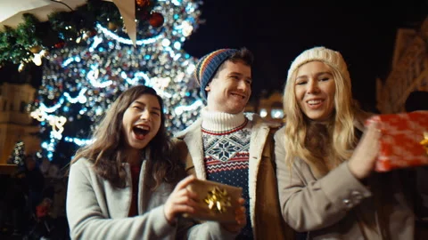 Three friends funny dancing with his gifts at christmas night at old town square 库存影片 166062437