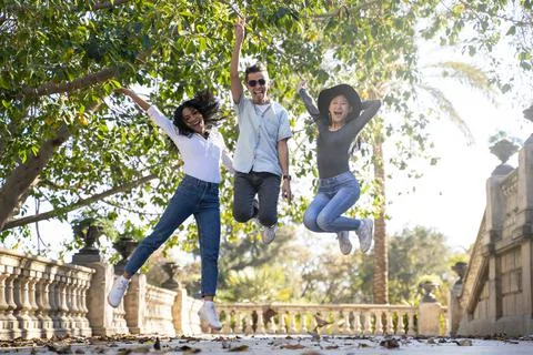 Three friends having fun jumping in the street looking at the camera Stock Photos