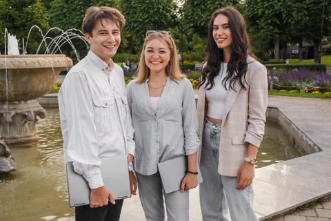 Three friends looking at camera together around park fountain 库存照片