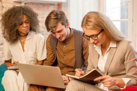 Three friends one of which is afro-american sitting in a nice location with the Stock Photos