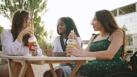 Three friends share lively conversation while sipping colorful drinks at a co Stock Photos