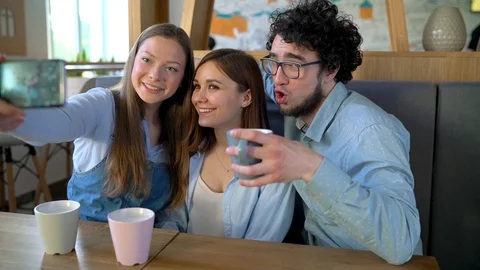 Three friends sit in a cafe, have fun communicating and make selfie Stock Footage 91287580