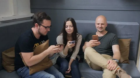 Three friends sit on sofa in studio and play with smartphones Stock Footage 67186226