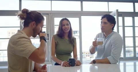 Three friends sitting at white counter, left man raising dark mug, catching up, Stock Footage 337944638