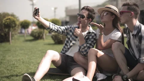Three friends take a selfie while sitting on the grass in a modern city Stock Footage 131244733