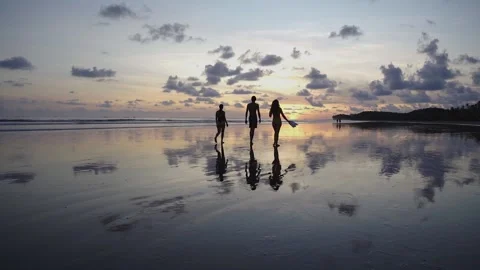Three friends walk on the beach over a beautiful sunset Stock Footage 151704813