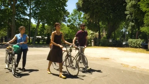 Three Friends Walking with Bycicles in a Park in Rome Video stock 77456360