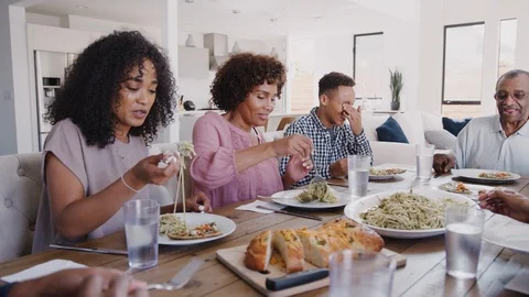 Three generation black family sitting at dinner table serving spaghetti, panning Stock Footage