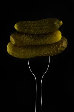 Three gherkins on a fork on a dark background Stock Photos