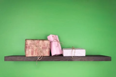 Three gift boxes on a dark color shelf with wood texture mounted on a green w 库存照片