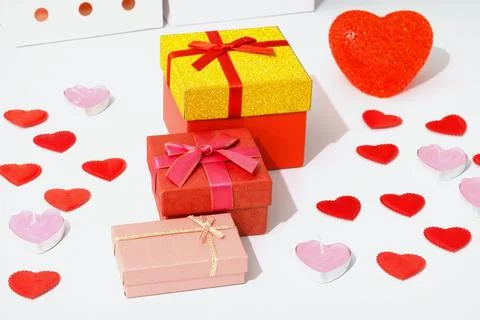 Three gift boxes in different colors are placed on a surface. Small heart d.. 스톡 사진