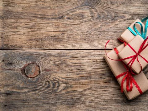 Three gift boxes of Kraft paper with ribbons on a brown wooden background, top Stock Photos