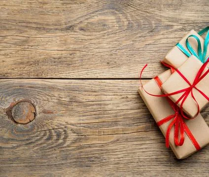 Three gift boxes of Kraft paper with ribbons on a brown wooden background, top Stock Photos