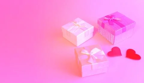 Three gift boxes with ribbon bows and two red hearts on a pink background. Va Stock Photos
