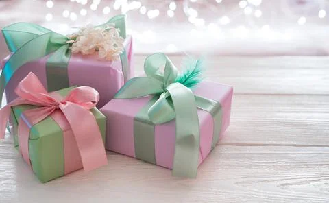 Three gift boxes with ribbons on a light background with a burning garland. Stock Photos