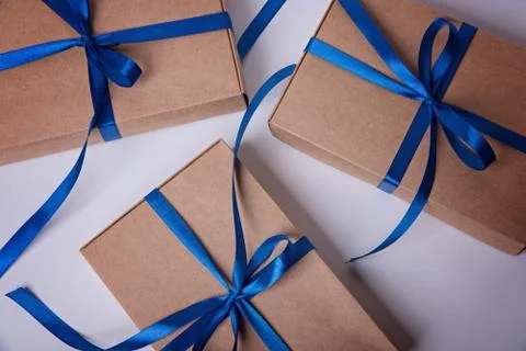 Three gift boxes wrapped in craft paper with a classic blue ribbons. Stock Photos