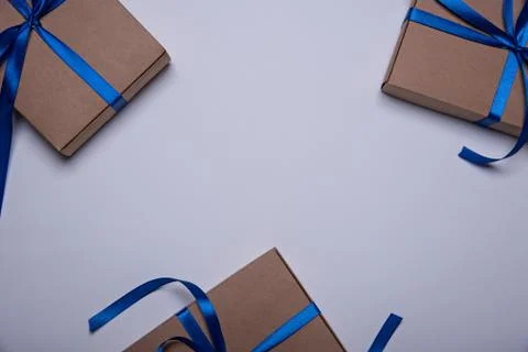 Three gift boxes wrapped in craft paper with a classic blue ribbons. Stock Photos