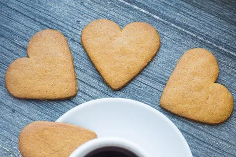 Three gingerbread heart shaped biscuits near border of white porcelain coffee 写真素材