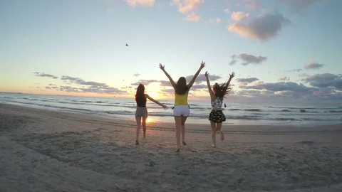 Three girlfriends running on a sandy beach towards the sea and playing with.. Stock Footage 71995766