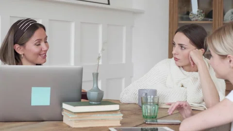 Three girlfriends sit at home at the table and talk about a new project Stock Footage 131846653