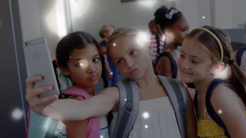Three girls aligning faces in school hall center extending phone causing sparkle Stockbeeldmateriaal 334182923