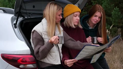 Three girls are reading a map. Friends are traveling by car in forest. Stock Footage 254289590