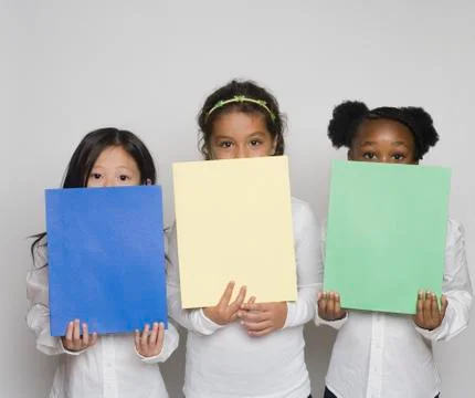Three girls holding up multi colored paper Stock Photos