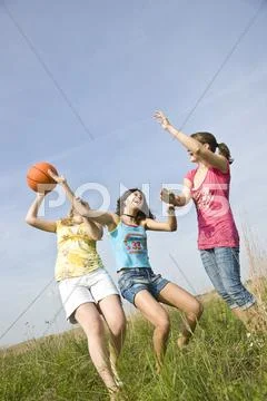 Three Girls Playing With A Basketball On A Meadow