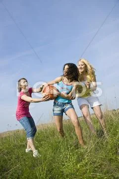 Three Girls Playing With A Basketball On A Meadow