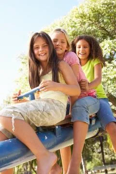 Three Girls Riding On See Saw In Playground Stock Photos
