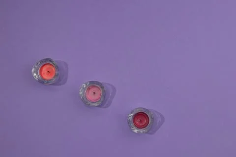 Three glass candlesticks with colored candles arranged in a line on a purpl.. Stock Photos