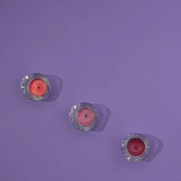 Three glass candlesticks with colored candles arranged in a line on a purpl.. Stock Photos