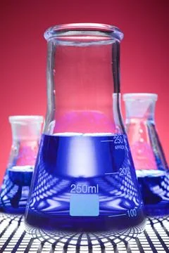 Three glass flasks placed in a laboratory table with blue liquid Stock Photos