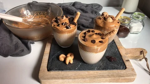 Three glasses with dalgona coffee decorated with different toppings. Hands ar Stock Footage 129221498
