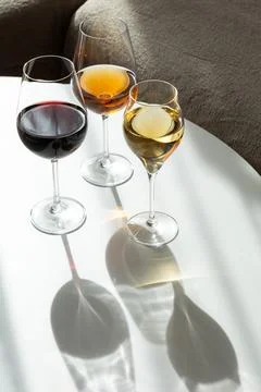 Three glasses filled with red white and rose wine on white table with shadows Stock Photos