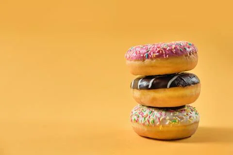 Three glazed donuts on a yellow background with copy space. Stock Photos